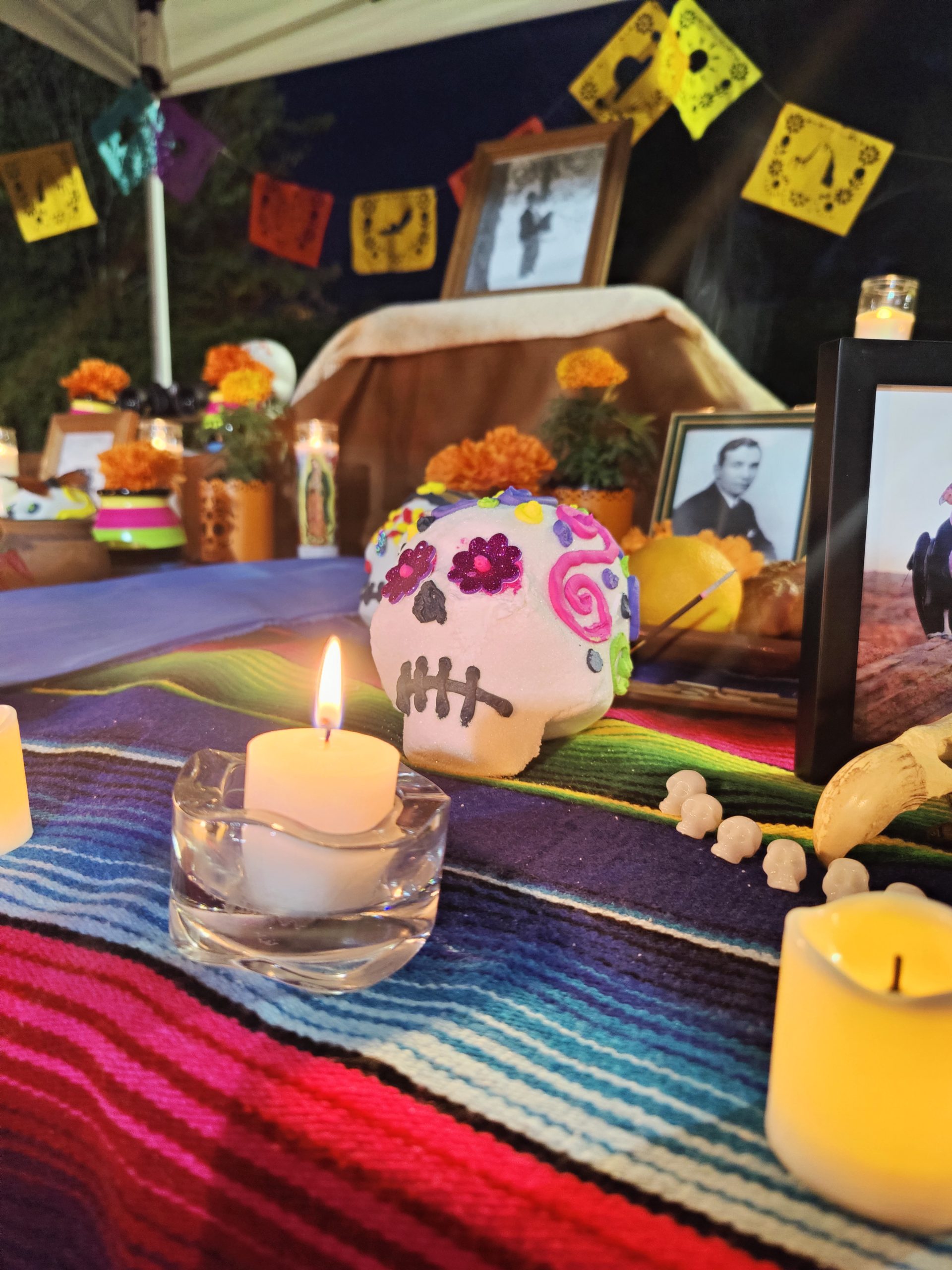 Lit candle in front of a sugar skull set up on a decorative table for Dia de los Muertos.