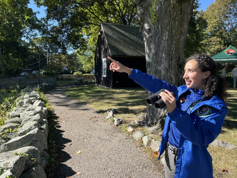 Intern outdoors holding binoculars and pointing at a bird in the sky.
